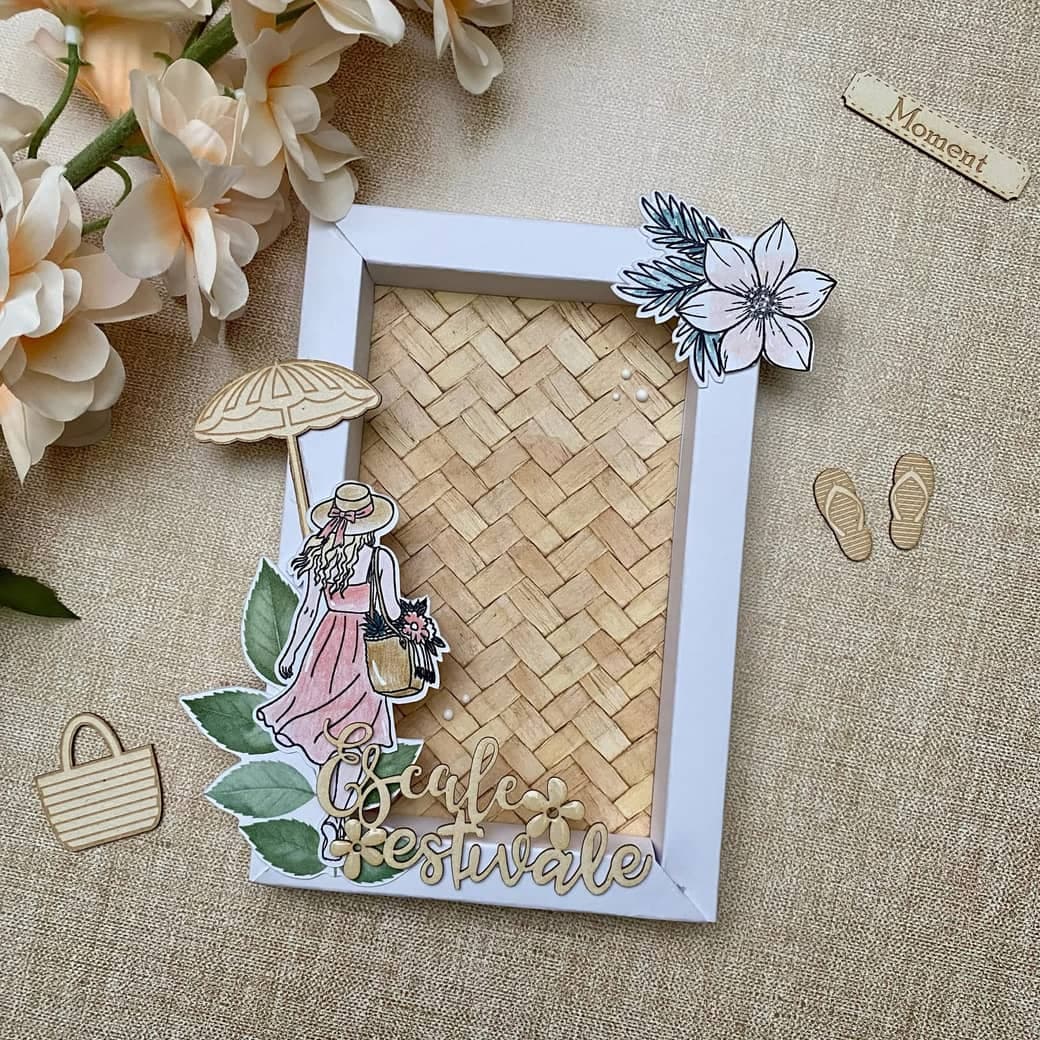 Cadre blanc au fond tressé, décoré d'une silhouette de femme au parasol et du mot « Escale estivale » découpé en bois.
